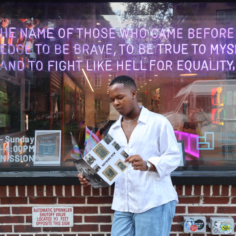 person reading in front of large storefront window with purple neon text above.